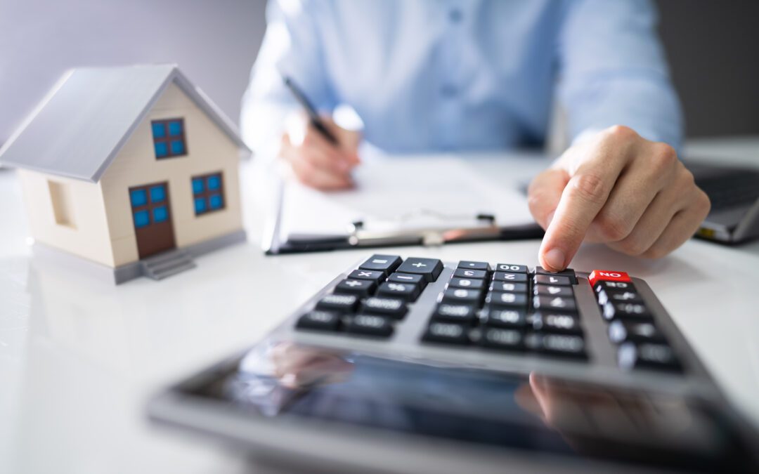 : Close-up of a person’s hand calculating a real estate property tax on wooden desk.