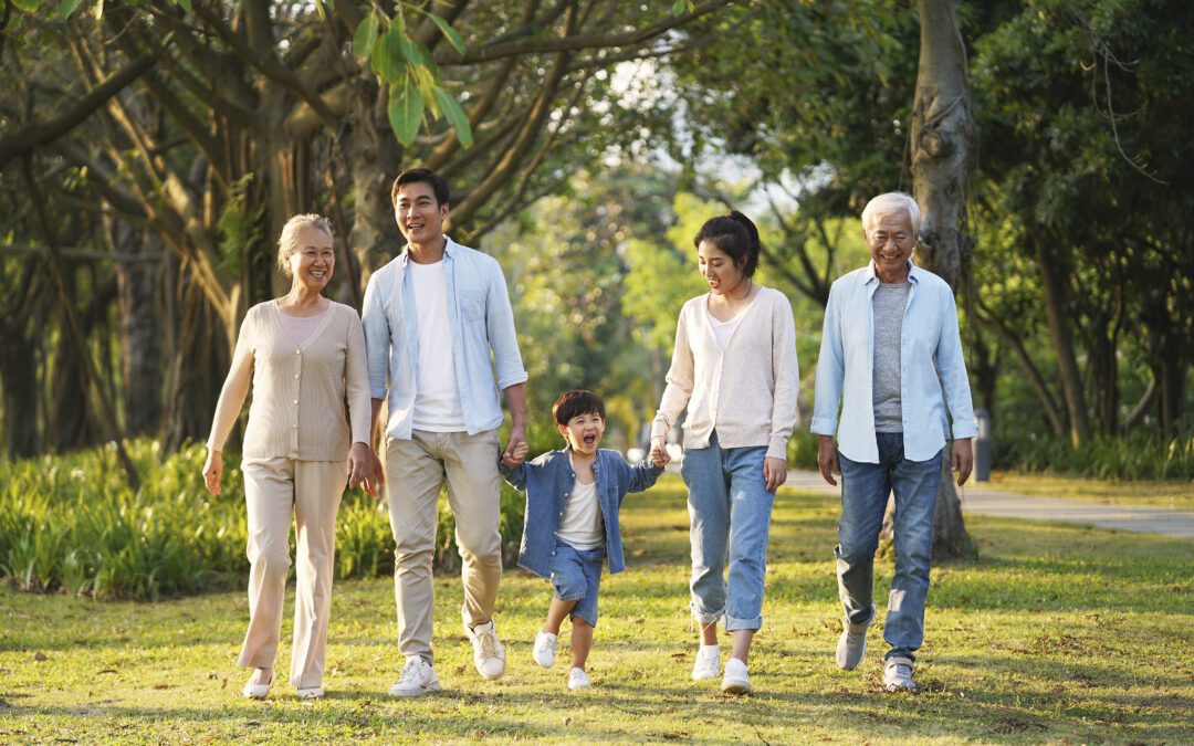 Three generations of a happy Asian family walk through a park together.