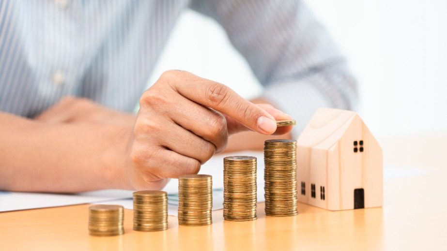 Someone stacking coins next to a wooden toy house